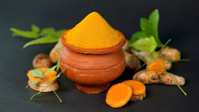 A cup full of turmeric powder surrounded by slices of turmeric root.