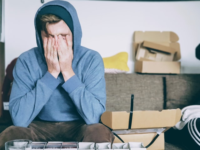 A man in a blue hoodie covering his face with his hands