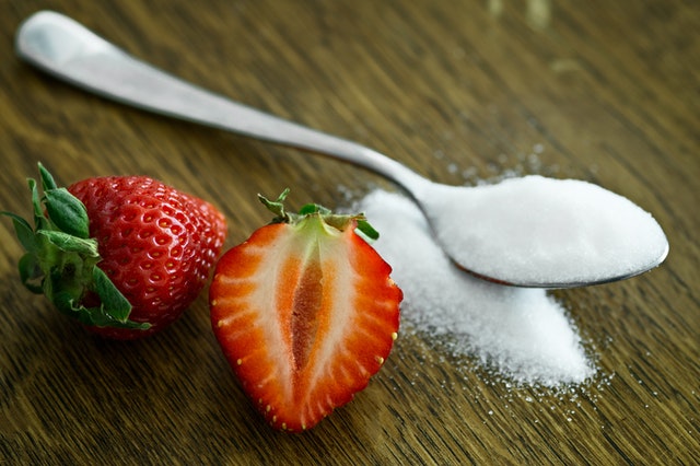 Two strawberries next to a spoon of sugar